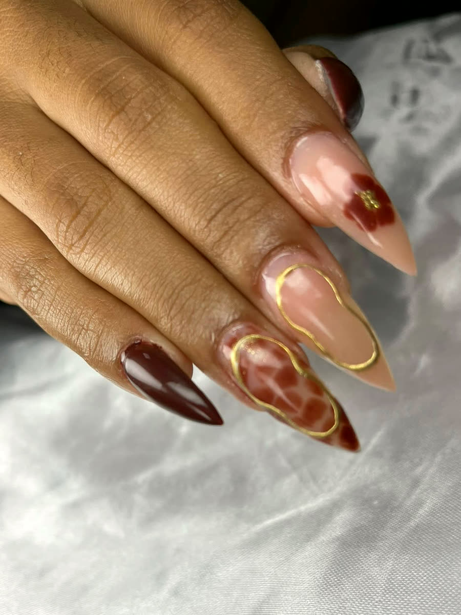 Unhas stiletto bordô e nude com arte em linhas douradas